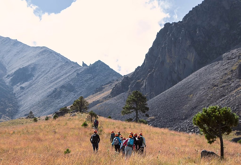 Hikers walking through a high-altitude trail surrounded by mountains and volcanic landscapes in Iztacc&iacute;huatl-Popocat&eacute;petl National Park, central Mexico.