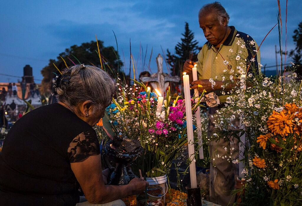 Elderly couple lighting candles and arranging flowers at a decorated grave in Mixquic during Day of the Dead celebration.
