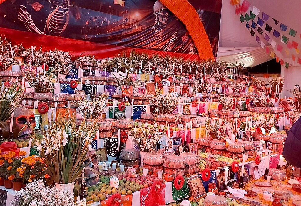 Large colorful Day of the Dead altar in Mixquic, filled with candles, flowers, food, photos, and traditional decorations.