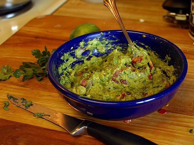 Fresh guacamole in mexico served in a blue bowl on a wooden table with lime and herbs, traditional mexican food enjoyed by travelers