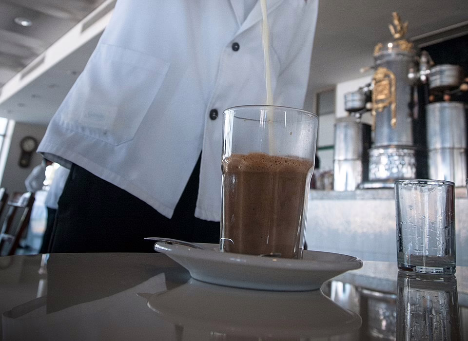 A glass of café lechero being served in Veracruz, with milk poured by a waiter inside a traditional café, showing the famous local coffee ritual.