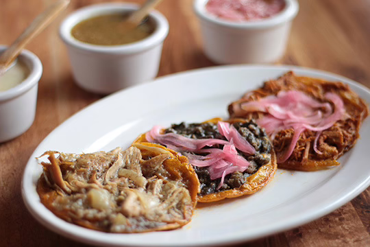 food in yucatan, traditional salbutes topped with shredded chicken, black beans, and pickled red onion on a white plate
