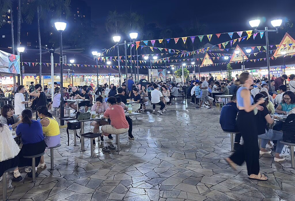 Nighttime market with colorful flags and busy food stalls. A lively atmosphere filled with people enjoying local street food. Singapore Cuisine
