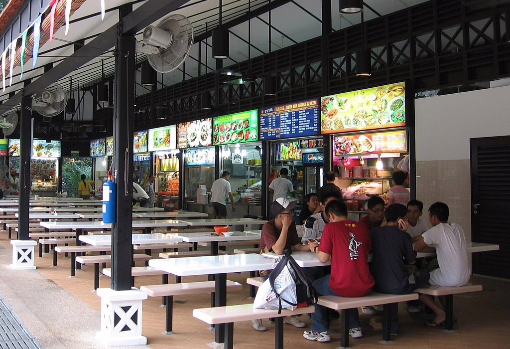 A food court with many stalls offering various dishes in Singapore. People enjoy meals in a casual setting. Singapore Cuisine.