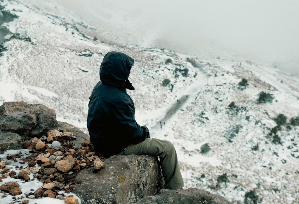 A person sitting on a rock in the snow, surrounded by a snowy landscape. Snow in Mexico, offering a peaceful mountain experience.