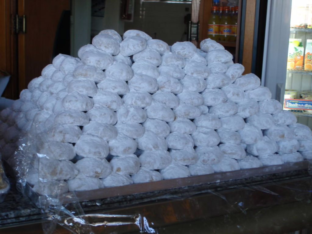 Traditional Greek kourabiedes stacked in a bakery, covered in powdered sugar, ready to be enjoyed during holidays or special occasions.