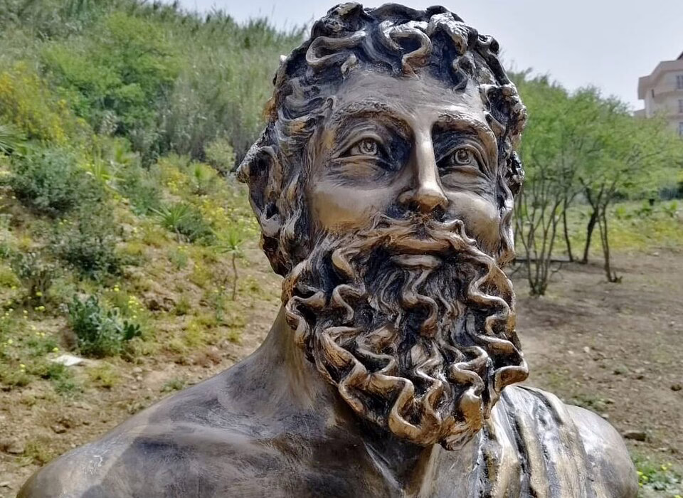 Bronze statue of Archestratus, ancient Greek writer and father of food literature, with greenery and trees in the background