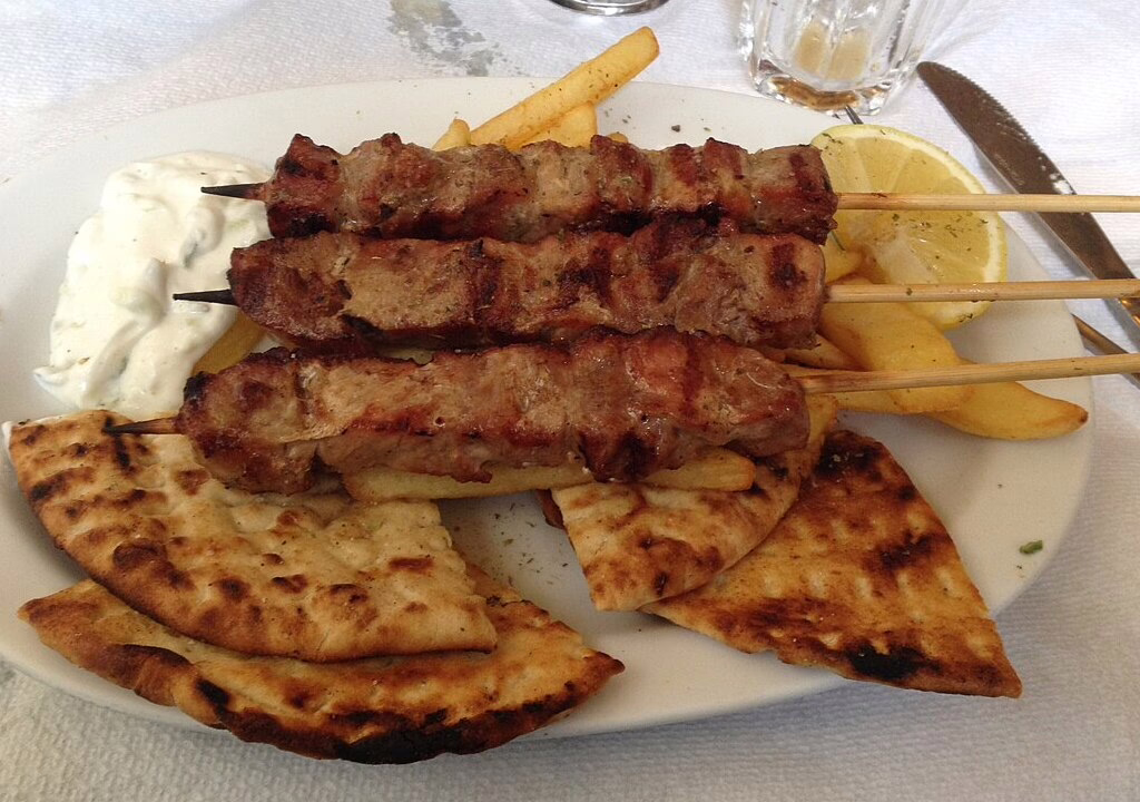 Greek souvlaki skewers served with pita bread, fries, tzatziki sauce, and lemon on a white plate in a traditional restaurant in Athens.