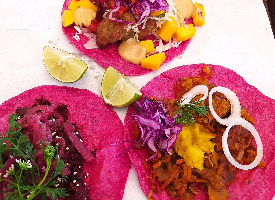 Three vibrant pink tacos with vegan fillings like onions, cabbage, mango, and lime slices, offering a colorful and tasty experience in Mexico City.