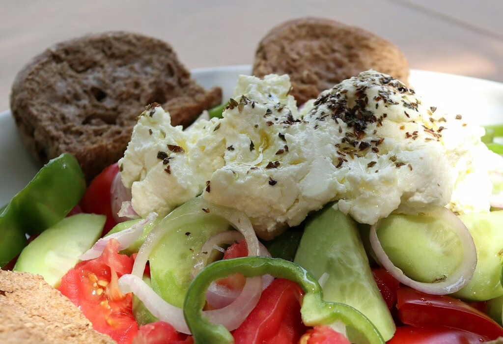 Greek salad with tomatoes, cucumber, onions, feta cheese, olive oil, and brown bread on a plate in Greece.