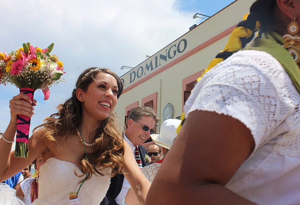A laughing bride holding a colorful bouquet during a traditional Oaxacan wedding parade called a Calenda.