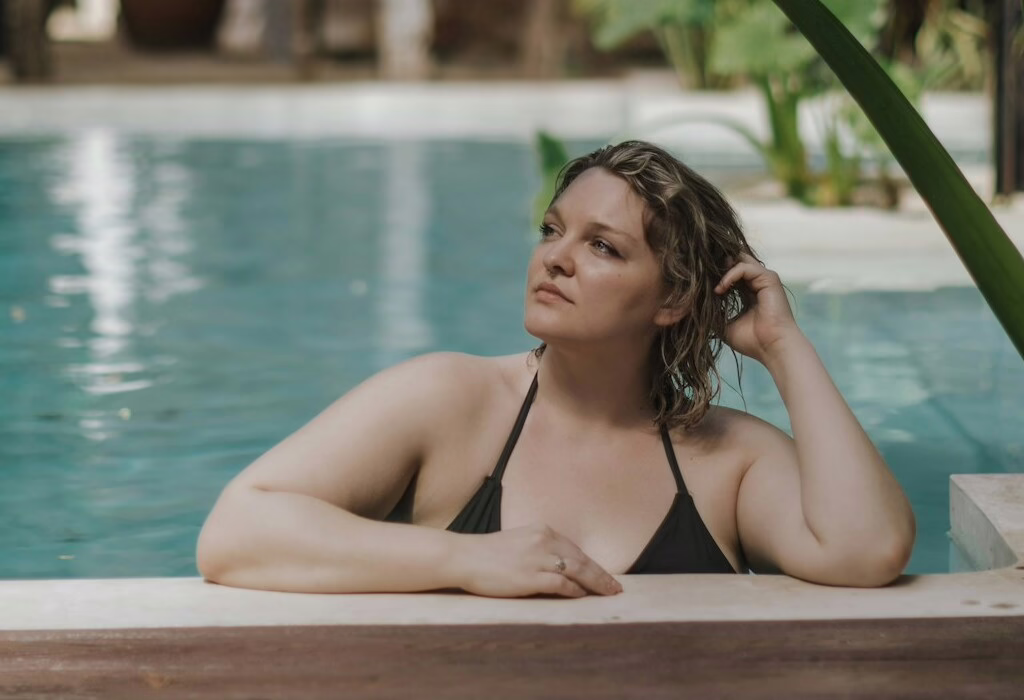 A woman relaxing in a blue swimming pool at a luxury spa resort with green tropical plants in the background.