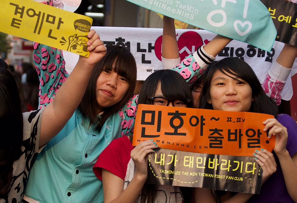 A group of enthusiastic K-pop fans holding colorful signs in support of their favorite idol, showcasing their excitement at a live event.