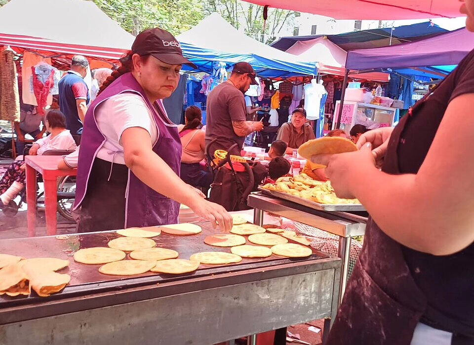 A woman prepares fresh tortillas at a bustling tianguis market, offering a taste of authentic Mexican street food.