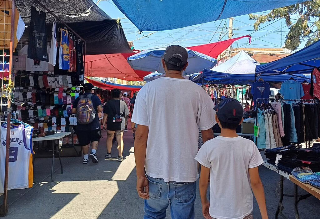 Father and son walking through a colorful outdoor market, exploring local shops at a tianguis in Mexico.