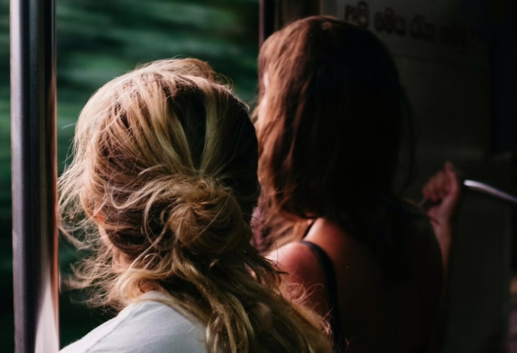 Two travelers by an open train doorway, wind in their hair, looking at a blurred green landscape, warm light suggesting motion, freedom, and an easy adventure.