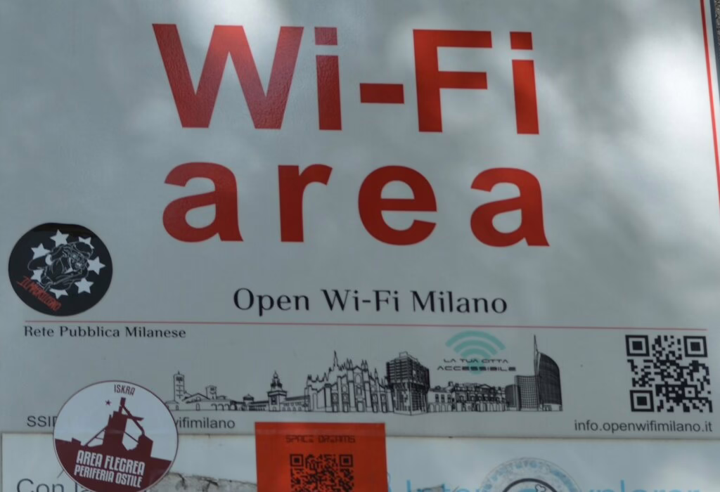 Wi-Fi area sign in Milan showing free public internet zone with skyline icons and QR code for Open Wi-Fi Milano.