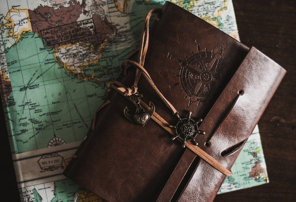 Leather travel journal with anchor charm on an old world map background, symbolizing adventure, exploration, and stories of journeys around the globe.