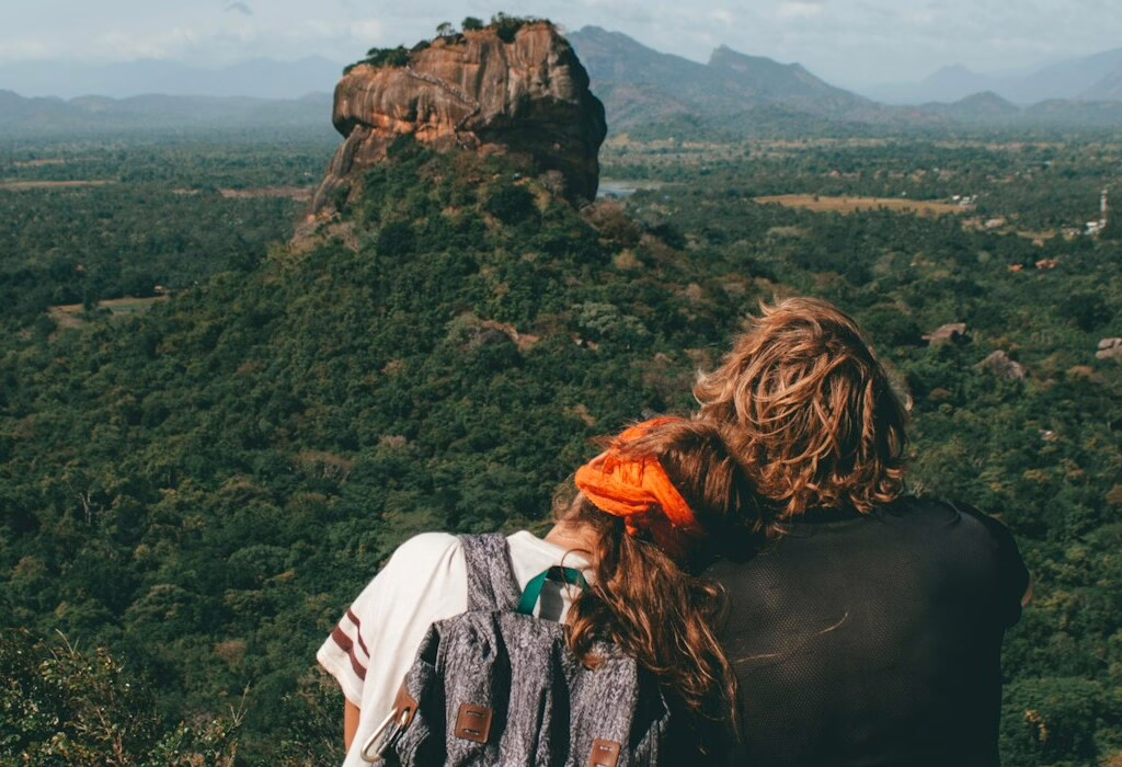 Couple sitting together with a view of Sigiriya Rock, surrounded by green forest and mountains, enjoying a peaceful travel moment in Sri Lanka.