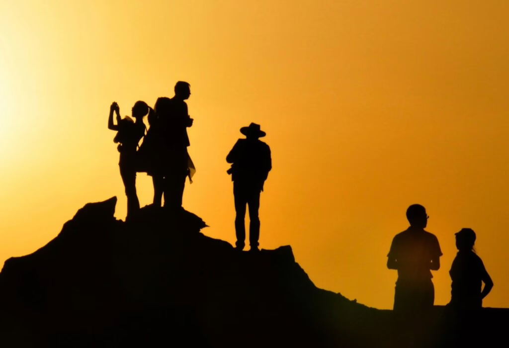 People standing on a hilltop at sunset, enjoying the golden sky with silhouettes creating a travel and adventure feeling.