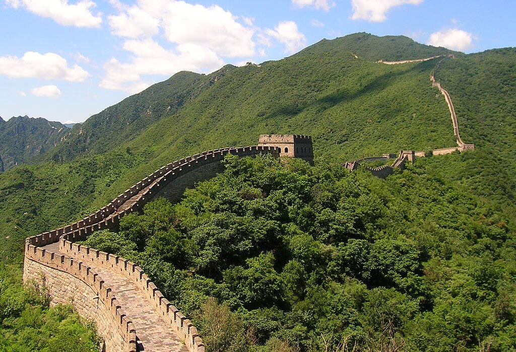 Summer greenery surrounds curving stones and a watchtower on the Great Wall.