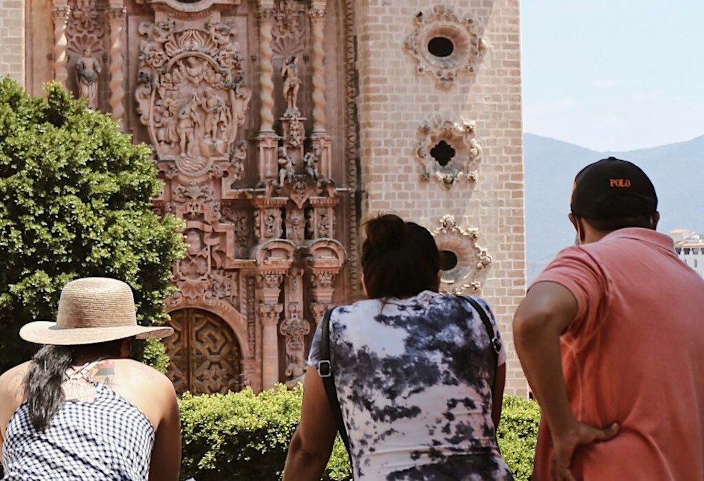 Travelers looking at ornate pink stone church in Taxco