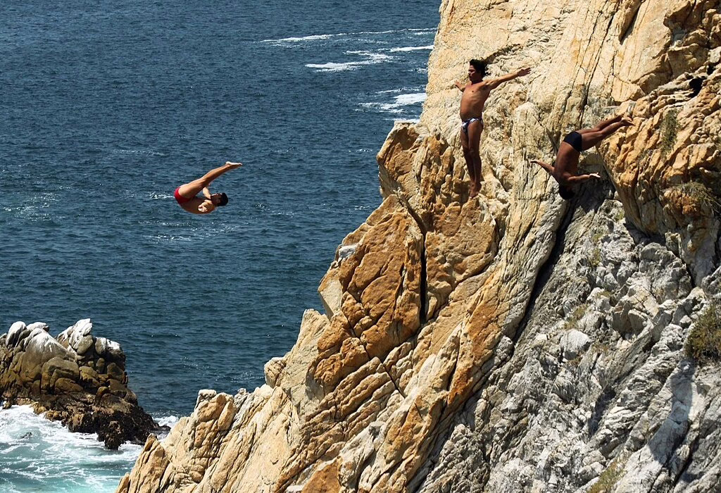 Cliff divers jumping off the rocky edges into the waters below in Acapulco, a popular adventurous activity in the city.