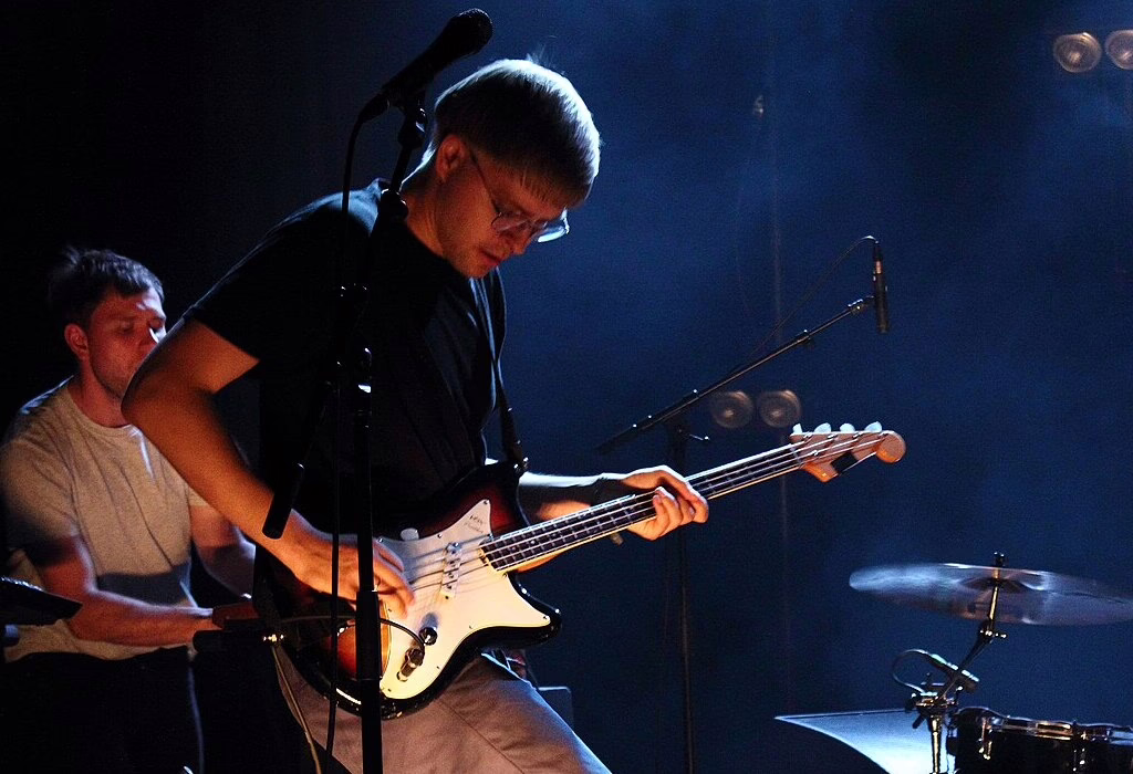 Musician playing bass guitar on stage with soft blue light during a live show in Mexico.