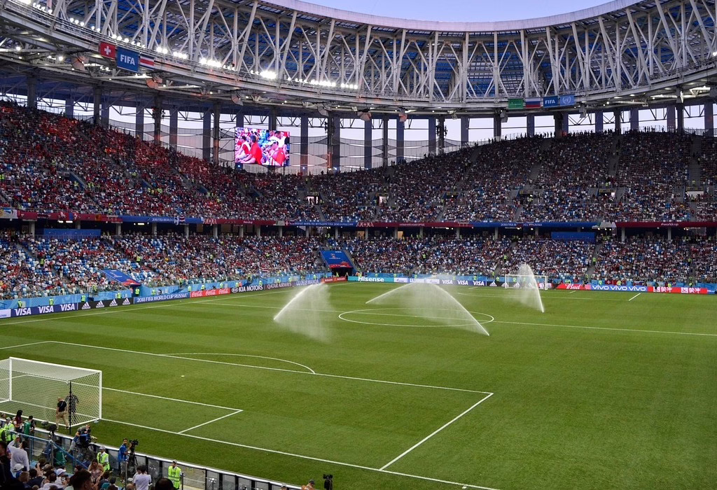 Grande estádio de futebol cheio de torcedores durante um jogo da Copa do Mundo no México, campo verde e aspersores de água antes do início da partida, Copa do Mundo no México