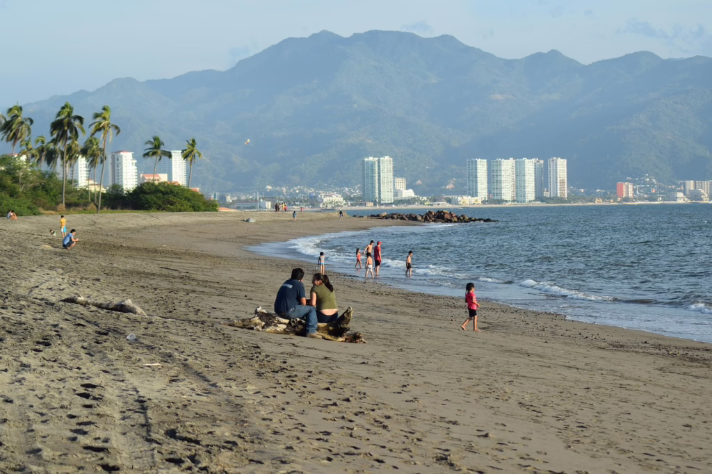 People enjoying a calm beach in Puerto Vallarta with mountains in the background, a safe coastal destination in Mexico