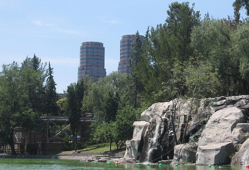 nature in mexico, lake and small waterfall in Chapultepec Park with trees and city buildings in the background