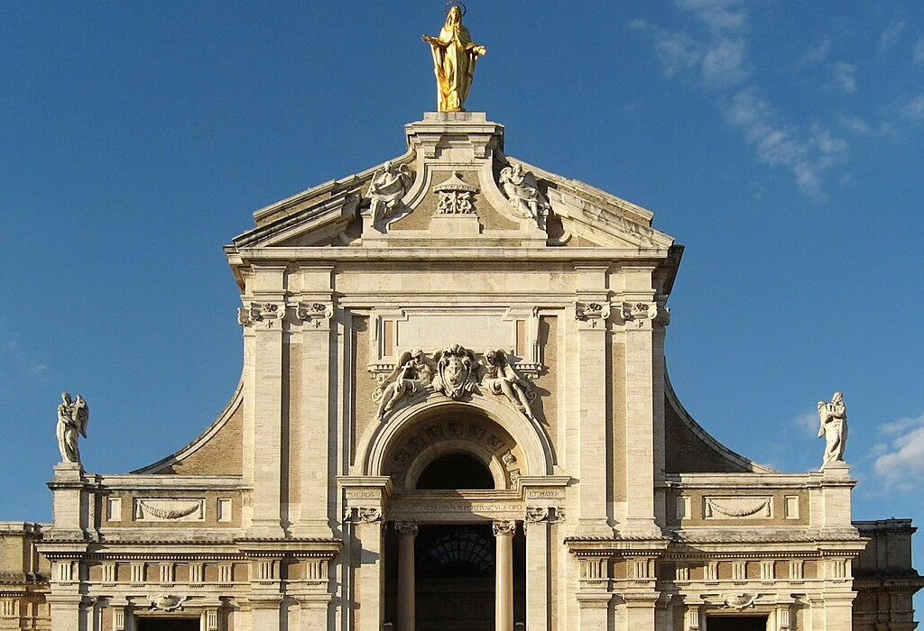 The grand facade of the Santa Maria degli Angeli church in Assisi, Italy, featuring a golden statue of the Virgin Mary and ornate architectural details