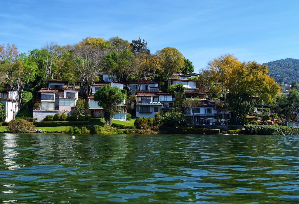 Lakeside villas and luxury houses with terraces surrounded by green trees on the shore of Lake Tequesquitengo, Morelos, under a clear blue sky.