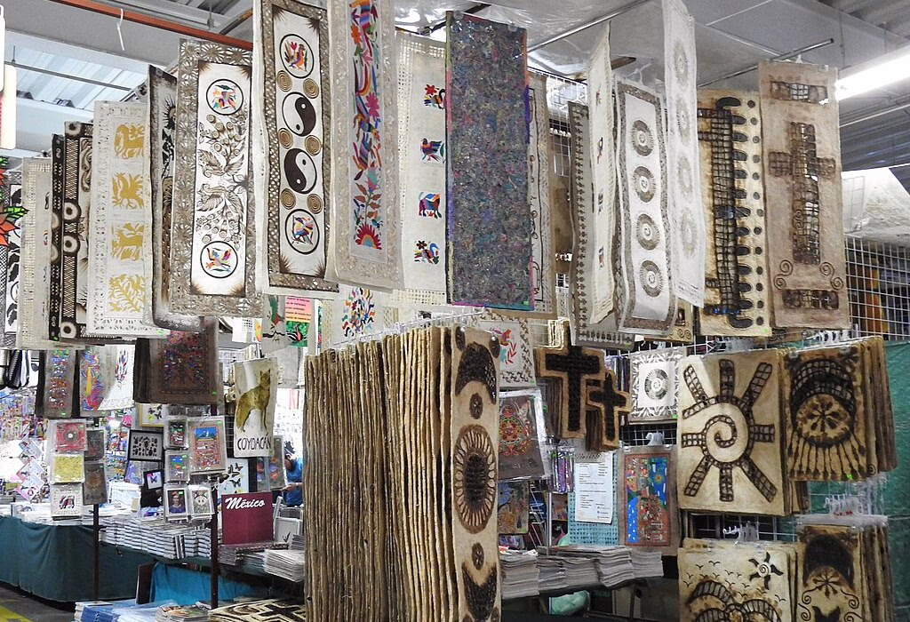 A wide angle view inside a large covered artisan market in Mexico City with many stalls and long textiles made from amate paper hanging from the ceiling.