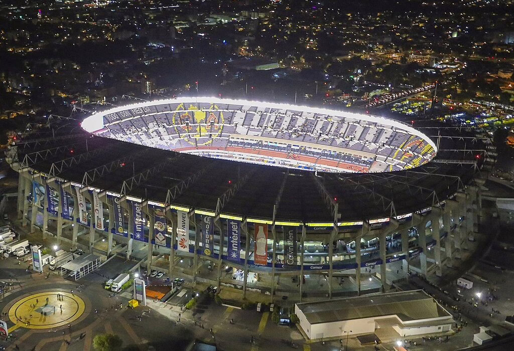High angle night view of the fully illuminated Estadio Azteca in Mexico City, a historic venue for the FIFA World Cup and other major events.