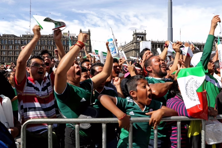 Mexican football fans screaming and celebrating a goal at the Zocalo Fan Zone. A young boy and adults cheering with passion during a World Cup match.