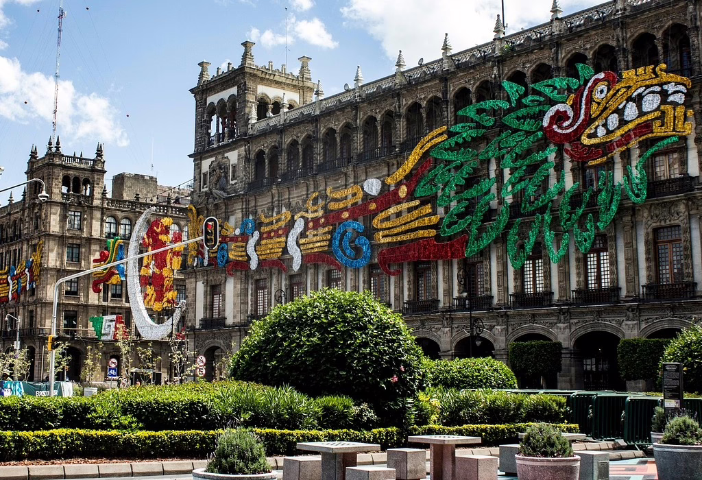View of the Zócalo in Mexico City with colonial buildings decorated for a national celebration. This area is the hub for hostels in mexico city and budget-friendly hotels for fans attending the 2026 World Cup opening match festivities.