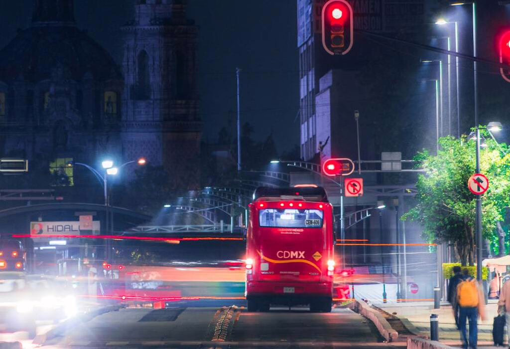 A red CDMX bus traveling safely on a well-lit city street at night, showing why Mexico City is safe for commuters.