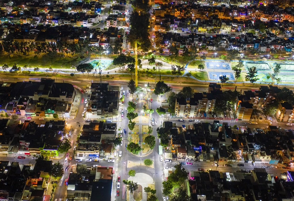 An aerial night view over Mexico City showing many busy streets with car lights, bright buildings, and a long park with green trees.